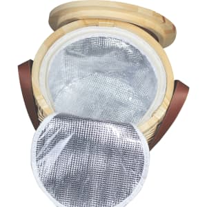 A wicker cooler basket in natural tones with a silver insulated interior and leather straps. It has a round lid.