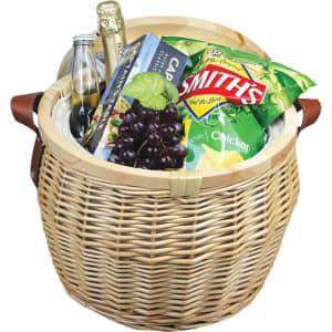 A wicker cooler basket in natural colour, filled with snacks, grapes, a drink bottle, and a magazine. It has leather handles.