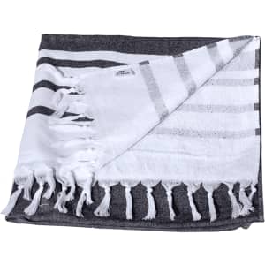 A Turkish beach towel with a dark grey and white striped design, featuring fringed edges and a small logo.