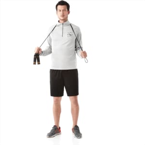 A man in a light grey quarter zip jumper holds a skipping rope, wearing black shorts and trainers.