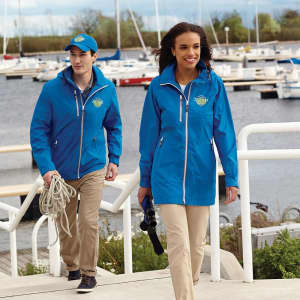 A blue rain jacket worn by a woman, paired with a blue cap and beige trousers, near a marina.