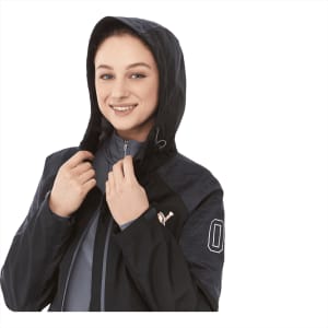 A woman smiles while wearing a black softshell jacket with a hood and a logo. The jacket has a stylish design.