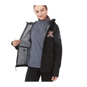 A woman wears a black softshell jacket open to reveal a grey interior. The jacket features a logo on the sleeve.