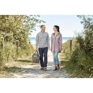 A grey and maroon women's knit zip hoody with a logo, worn with light jeans and brown boots, set against a coastal pathway.