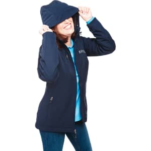 A woman wearing a navy softshell jacket with a hood, smiling and playfully pulling it over her face.