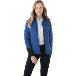A woman wearing a blue quilted insulated jacket with a black collar and branding.