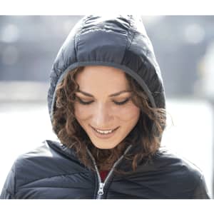 A woman wearing a navy insulated jacket with a hood, smiling gently in an outdoor setting.
