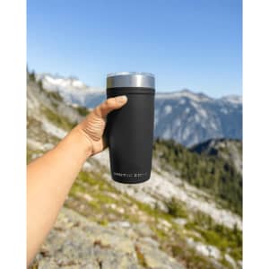 A drink bottle with a matte black finish and a silver lid, held against a mountainous landscape.