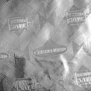 A silver textured surface featuring a diamond pattern with branding logos embossed throughout.