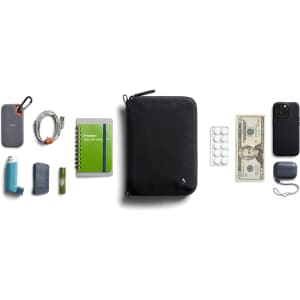 A black toiletry bag with various items including a drink bottle, notebook, cash, and an inhaler. It has a logo.