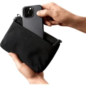 A black toiletry bag being held, with a smartphone and pen inside. The bag features a zip closure and a logo.