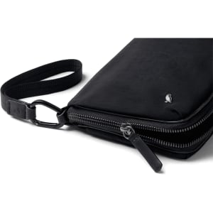 A black toiletry bag with a zippered closure and a detachable strap, featuring a discreet logo.