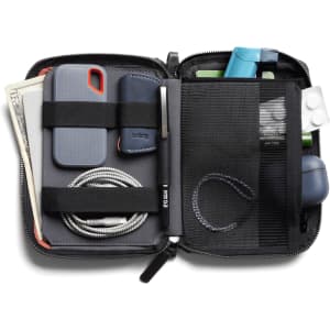A compact, black toiletry bag containing a phone, cash, cables, a pen, and various small accessories. It features organisational straps.