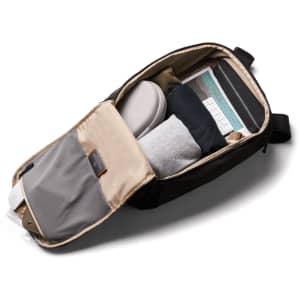 A black backpack partially unzipped, revealing neatly packed items including clothing, a laptop, and other accessories.