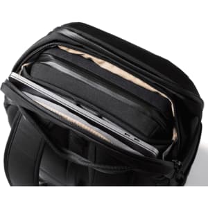 A black backpack with a zippered compartment showcasing a laptop and padded interior. It features a logo.