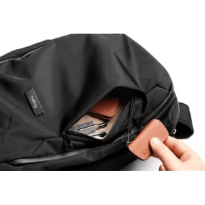 A black backpack features an open pocket with leather tags and various items inside, showcasing its organisational capacity.