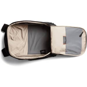 A black backpack with a beige interior and a grey compartment, featuring a logo on the outside.