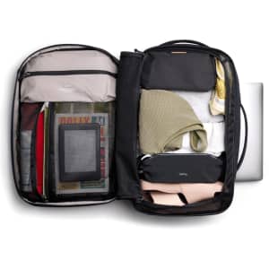 A black backpack with various items packed inside, including clothing, a laptop, and storage pouches in neutral tones.
