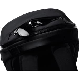 A black backpack with a zippered compartment, containing a pair of sunglasses. It features a logo on the exterior.