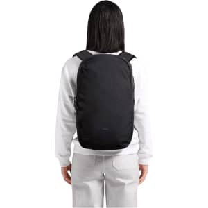 A black Bellroy Via Backpack 20L is worn on the back of a person in casual attire, showcasing its sleek design.