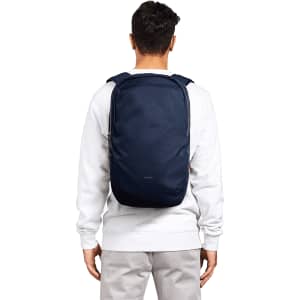 A person wearing a navy blue backpack, featuring padded shoulder straps and a simple design. The backpack has a logo.