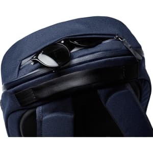 A navy Bellroy Via Backpack with a zippered compartment featuring sunglasses on top. The bag has a sleek, textured finish.