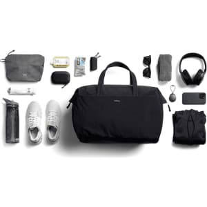 A black duffel bag surrounded by a water bottle, shoes, a hoodie, headphones, sunglasses, and various accessories.