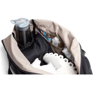 A black duffel bag opened to reveal a drink bottle, athletic shoes, and various smaller items inside.