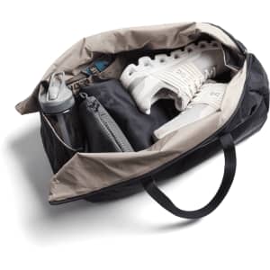 A black and beige duffel bag containing a water bottle, shoes, and a grey pouch. The bag has a logo.