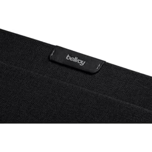 A black laptop sleeve made from textured fabric, featuring a small logo tag.