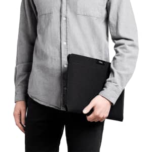 A laptop sleeve in black held by a person wearing a grey shirt, showcasing a sleek and minimalist design.