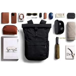 A black rolltop backpack surrounded by various items including sunglasses, a water bottle, tech accessories, and a book.