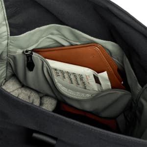 A grey interior of a bag features a brown wallet, a zipped pouch, and a rolled sweater. The bag has a branding logo.