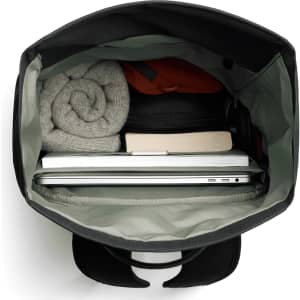 A black rolltop bag with a grey interior, containing a laptop, a book, and rolled clothing.