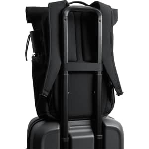 A black rolltop backpack is secured on a black suitcase, featuring padded straps and a side pocket.