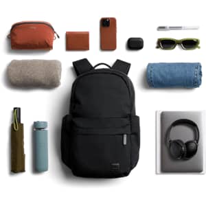 A black backpack surrounded by a drink bottle, sunglasses, a blanket, denim, headphones, and other accessories.