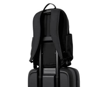 A black backpack rests on top of a black suitcase, with adjustable straps and side pockets visible.