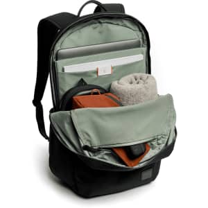 A black daypack with a green interior, featuring compartments for a laptop, a towel, and a small pouch.