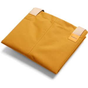 A mustard yellow tote bag with two straps, featuring a logo. The bag is folded and lying flat.
