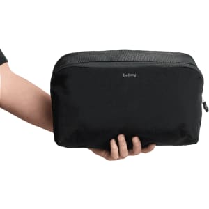 A black packing cube held in a hand, featuring a mesh panel and branded logo.