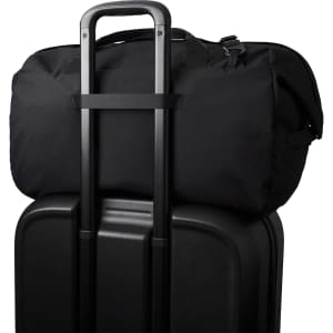 A black duffel bag sits on top of a black suitcase, featuring a trolley handle for easy transport.