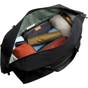 A black duffel bag open to reveal neatly packed items, including clothing and accessories in various colours.