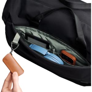 A close-up of a black duffel bag's interior, featuring a blue headset, a gadget, and a brown leather keychain.