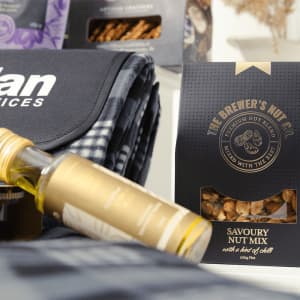 A drink bottle, a picnic blanket, and a Savoury Nut Mix packaged in a black box. The blanket features a checkered pattern.