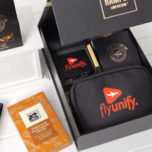 A black gift box contains a branded tech kit, featuring a black pouch, notebook, pen, and snacks.