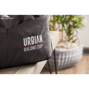 A dark grey duffel bag with a logo, placed on a table beside a potted plant and woven basket.