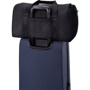 A black duffel bag rests on top of a dark blue suitcase, featuring straps and a handle.