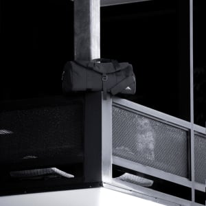A black duffel bag rests on a balcony railing, featuring a logo and sturdy handles.