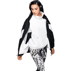A woman wearing a black and white jacket and patterned leggings, listening to headphones. The product features a logo.