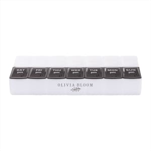 A clear pill case with eight compartments labelled for days of the week, featuring black lids and a logo.